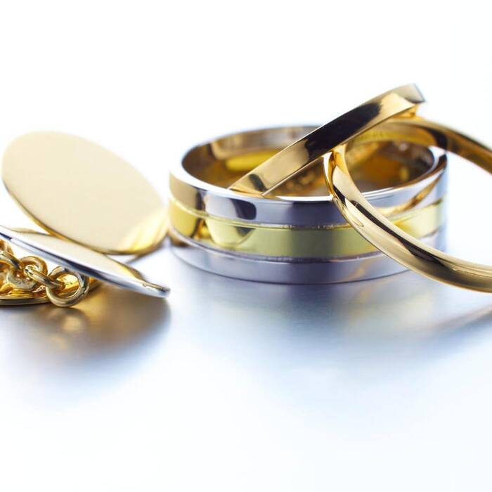 A collection of polished Welsh gold jewellery featuring a pair of round gold cufflinks, a wide two-tone gold and silver wedding band, and two slim, high-polish gold rings.