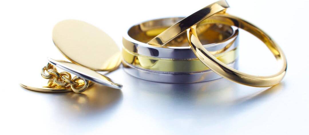A collection of polished Welsh gold jewellery featuring a pair of round gold cufflinks, a wide two-tone gold and silver wedding band, and two slim, high-polish gold rings.