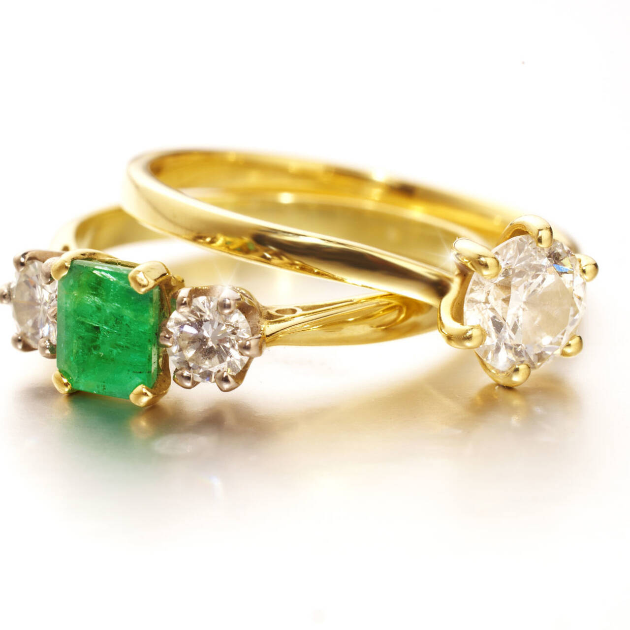 A matching pair of handcrafted gold rings featuring a vibrant emerald cut stone, diamond accents, and a classic solitaire engagement ring.