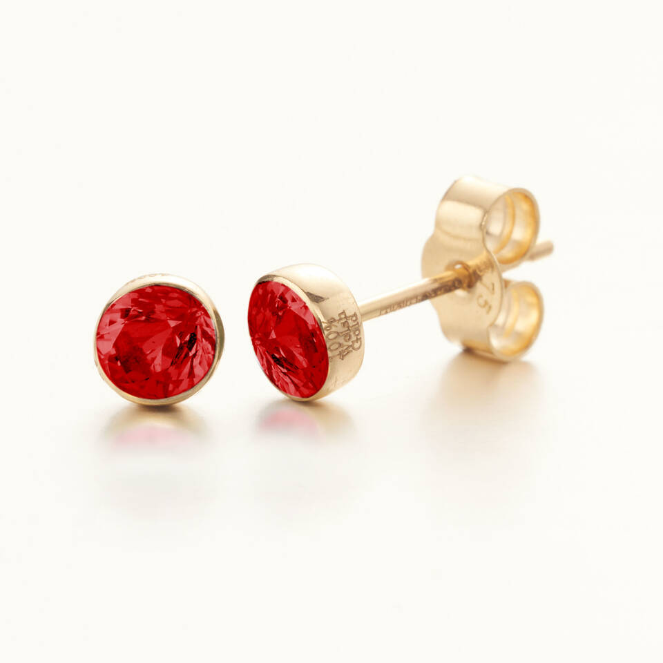 A pair of vibrant red ruby stud earrings set in 100% Welsh gold bezel mounts, featuring a polished finish and clear authenticity engravings on the side for a July birthday.