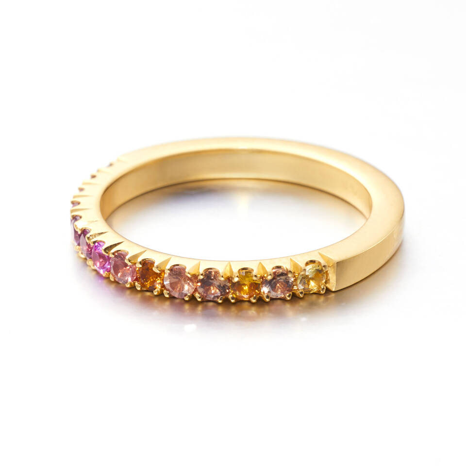 A polished yellow gold band featuring a pavé-set gradient of gemstones transitioning from vibrant pink rubies to warm orange and yellow sapphires.