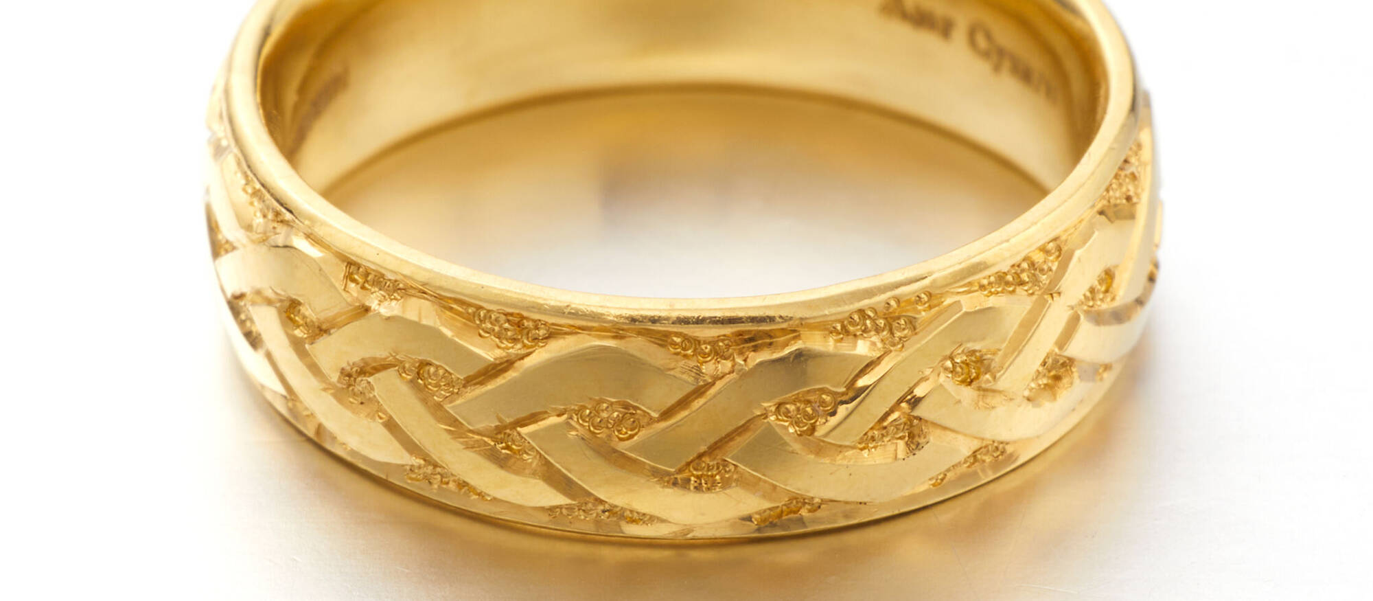 Close-up of a handcrafted gold ring showcasing precision-engraved interlaced knotwork and a smooth, polished inner surface for a personalised experience.