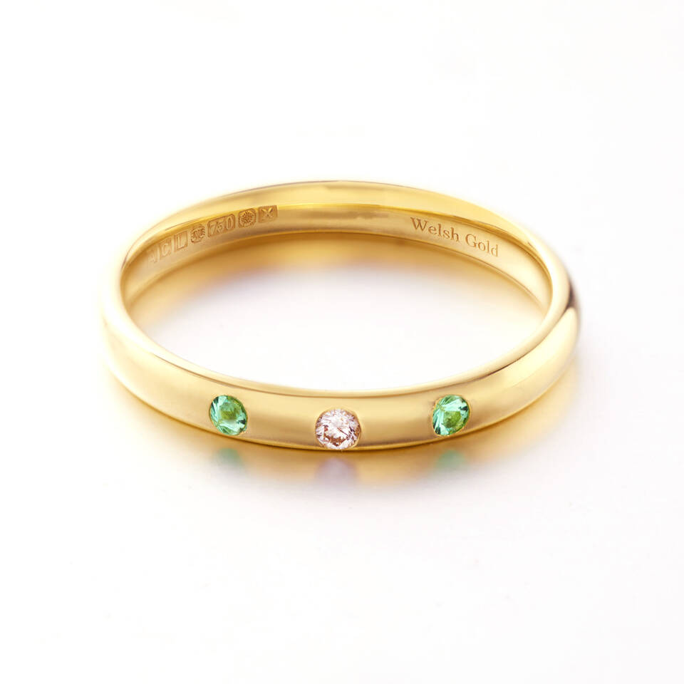 Elegant Welsh Gold band set with emeralds and diamonds, displaying the brand's signature hallmarking for authenticity.