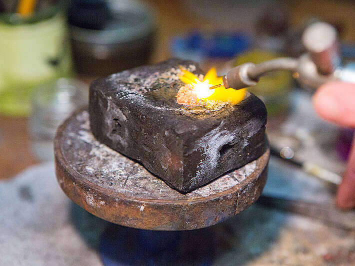 Close-up view capturing the moment raw gold begins to glow and liquify under intense heat during the traditional smelting stage of jewellery making.