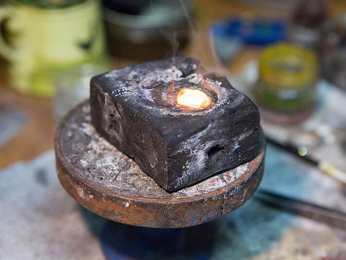 The result of the smelting process showing a white-hot, liquified bead of gold as it begins to solidify into a workable shape on the artisan's workbench.