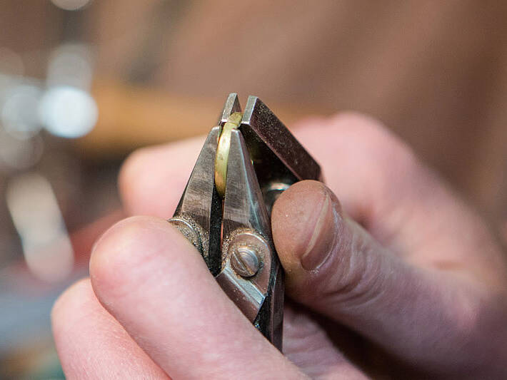 Handcrafting a Welsh gold wedding ring: an artisan uses specialised pliers to align the metal joint, a key step in creating a high-quality, seamless bespoke band.