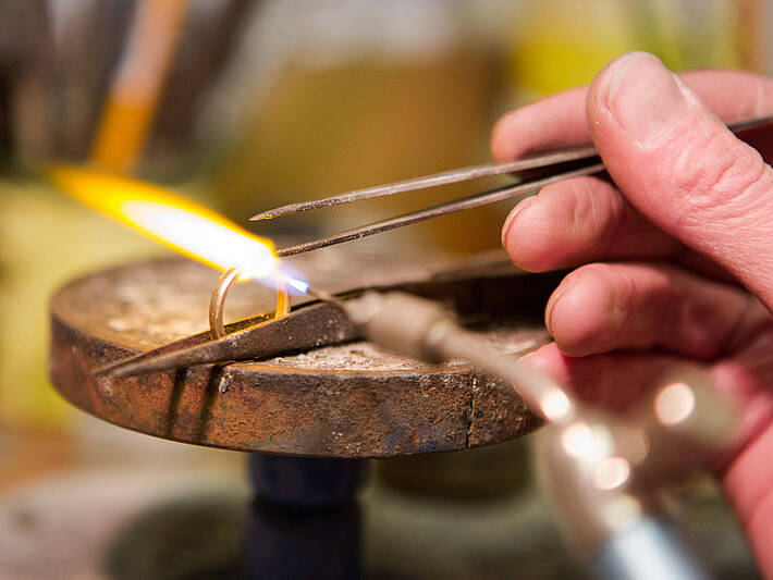 Master goldsmith hand-soldering a precious gold ring during a workshop repair