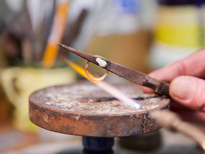 Detailed view capturing the glowing metal and the precision of the flame during the soldering stage of a handcrafted gold ring.