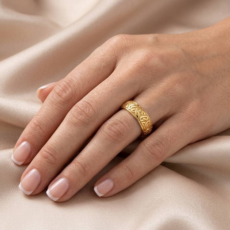 Close-up shot of a 5.7mm 100% Welsh gold Triquetra Celtic ring worn on a woman's ring finger against soft silk fabric.