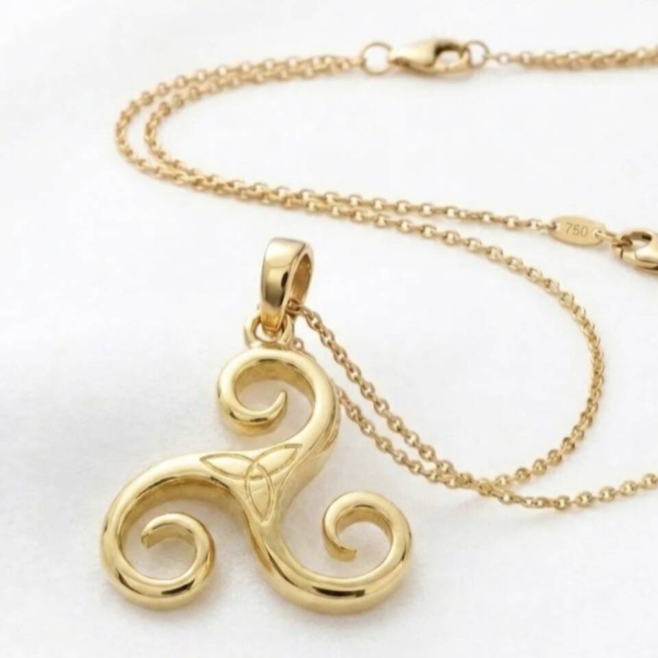 Close-up of a high-polish Welsh gold Celtic pendant showing the "750" purity hallmark on the chain's tag and the intricate curved details of the triskele design.