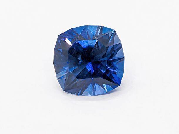 A vivid blue sapphire gemstone on a white background, showing its intricate facets and small details