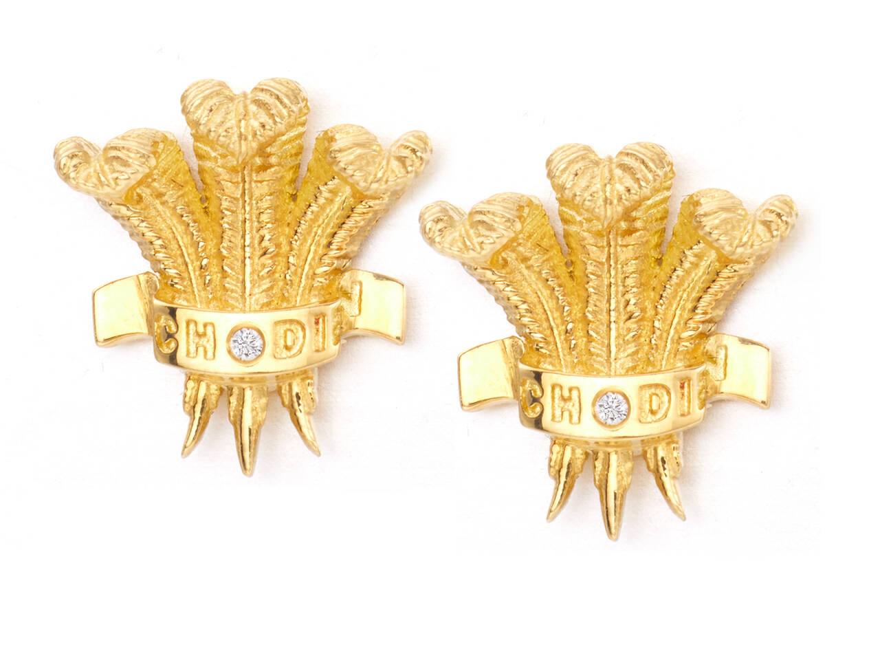 A top-down studio shot showing a pair of yellow gold earrings shaped like the Prince of Wales three-feather crest, with "CHODI" engraved on the ribbon and a central sparkling diamond.