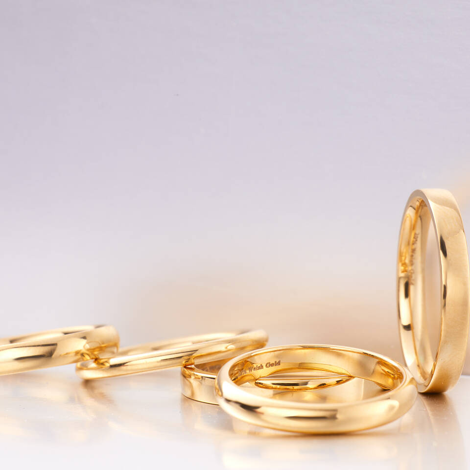 A group of polished gold wedding rings in various profiles, with a close-up on the internal "Welsh Gold" engraving and hallmark on a high-shine band.
